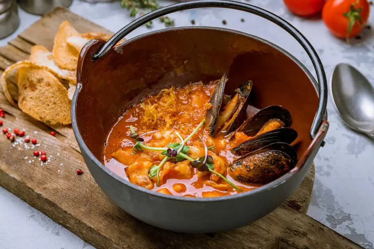 Un delicioso suquet de peix, con mejillones y gambas en una cazuela de barro, acompañado de tostas.