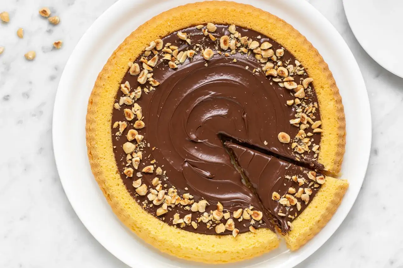 Crostata mascarpone e nutella con nocciole tritate. Una fetta è stata tagliata, invitando a gustare questa delizia.