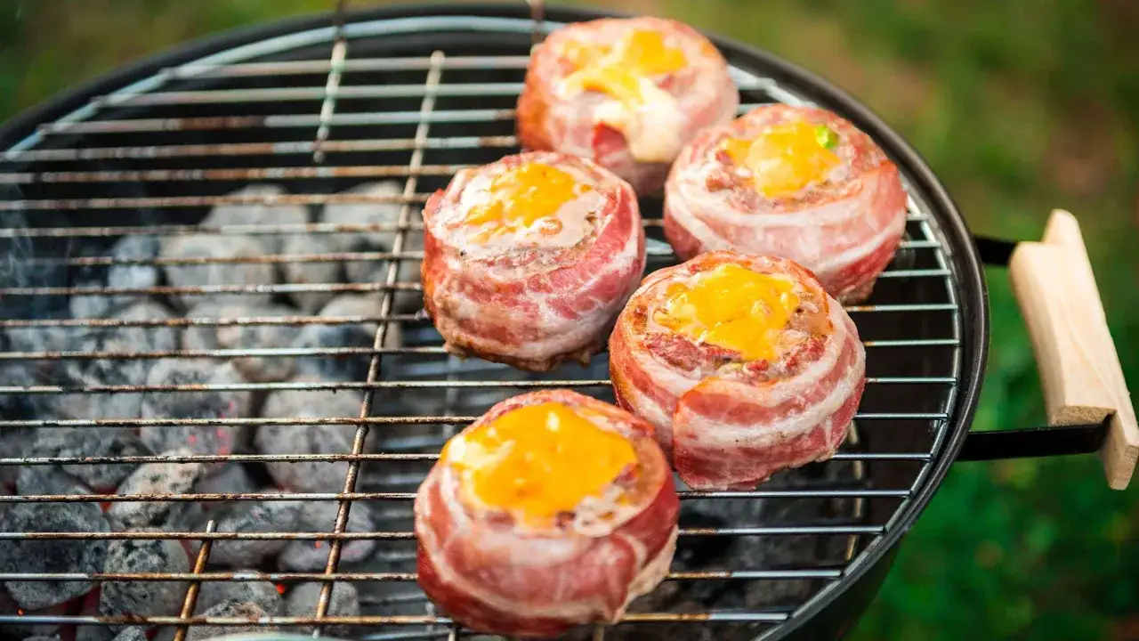 Cinq boules de viande envelopp&eacute;es de bacon, garnies de fromage fondu, sur un barbecue pour une cuisson indirecte parfaite.