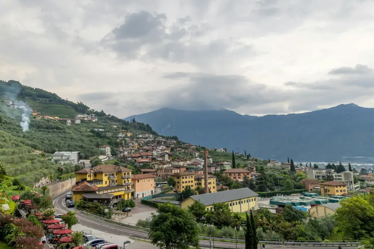 Paesaggio collinare con case colorate e uliveti, sullo sfondo montagne nebbiose. Un luogo ideale per visitare il giardino botanico del Lago di Garda.