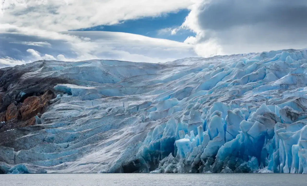 Glaciar azul intenso en la patagonia chilena, con rocas oscuras y cielo nublado.