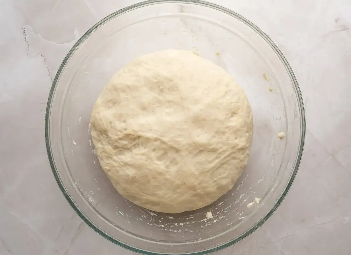 En perfekt deg för ditt pizzadeg recept, redo att jäsa i en glasskål.