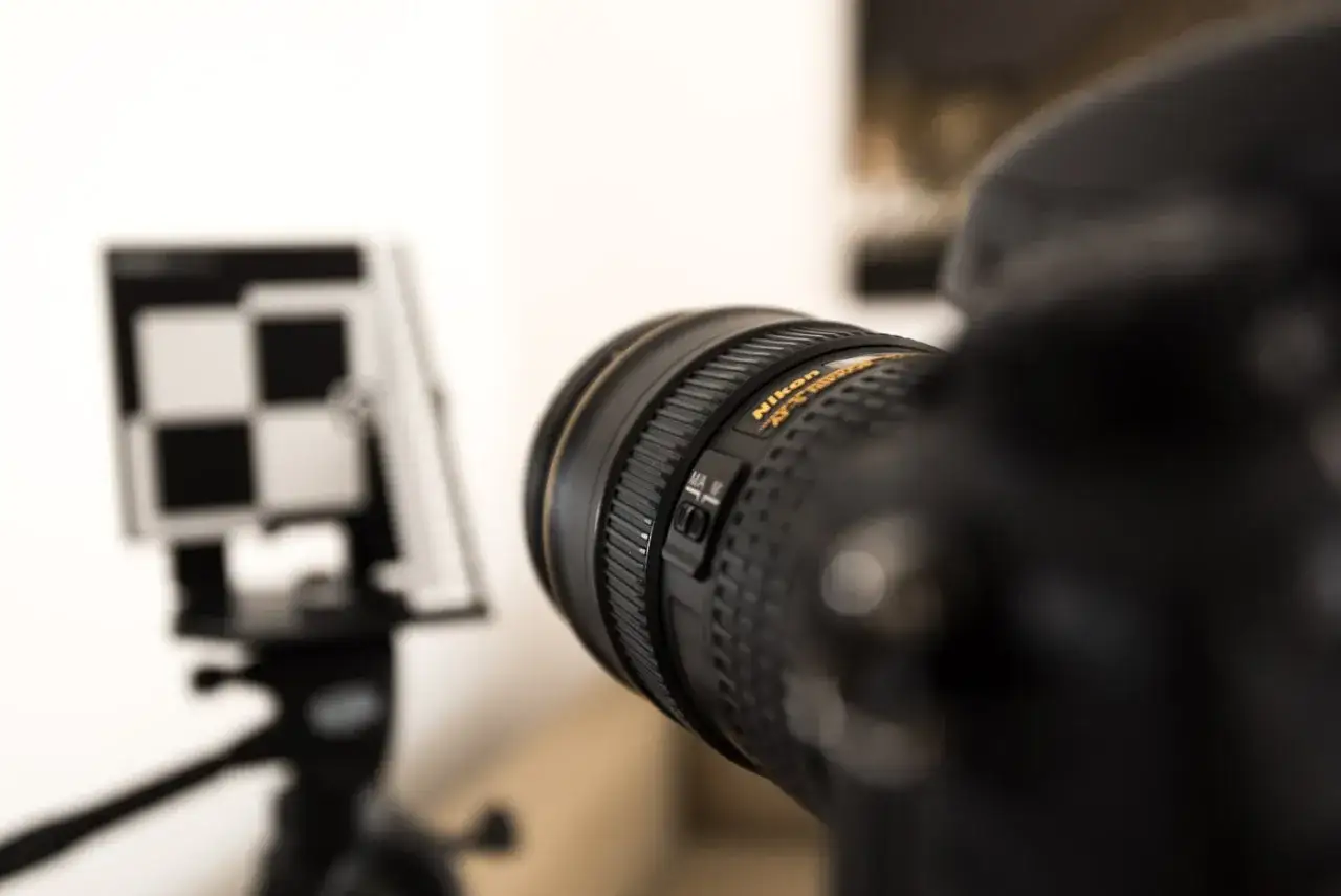 Objectif Nikon en gros plan, avec une mire de mise au point floue en arrière-plan. Le réglage de l'auto focus est visible.