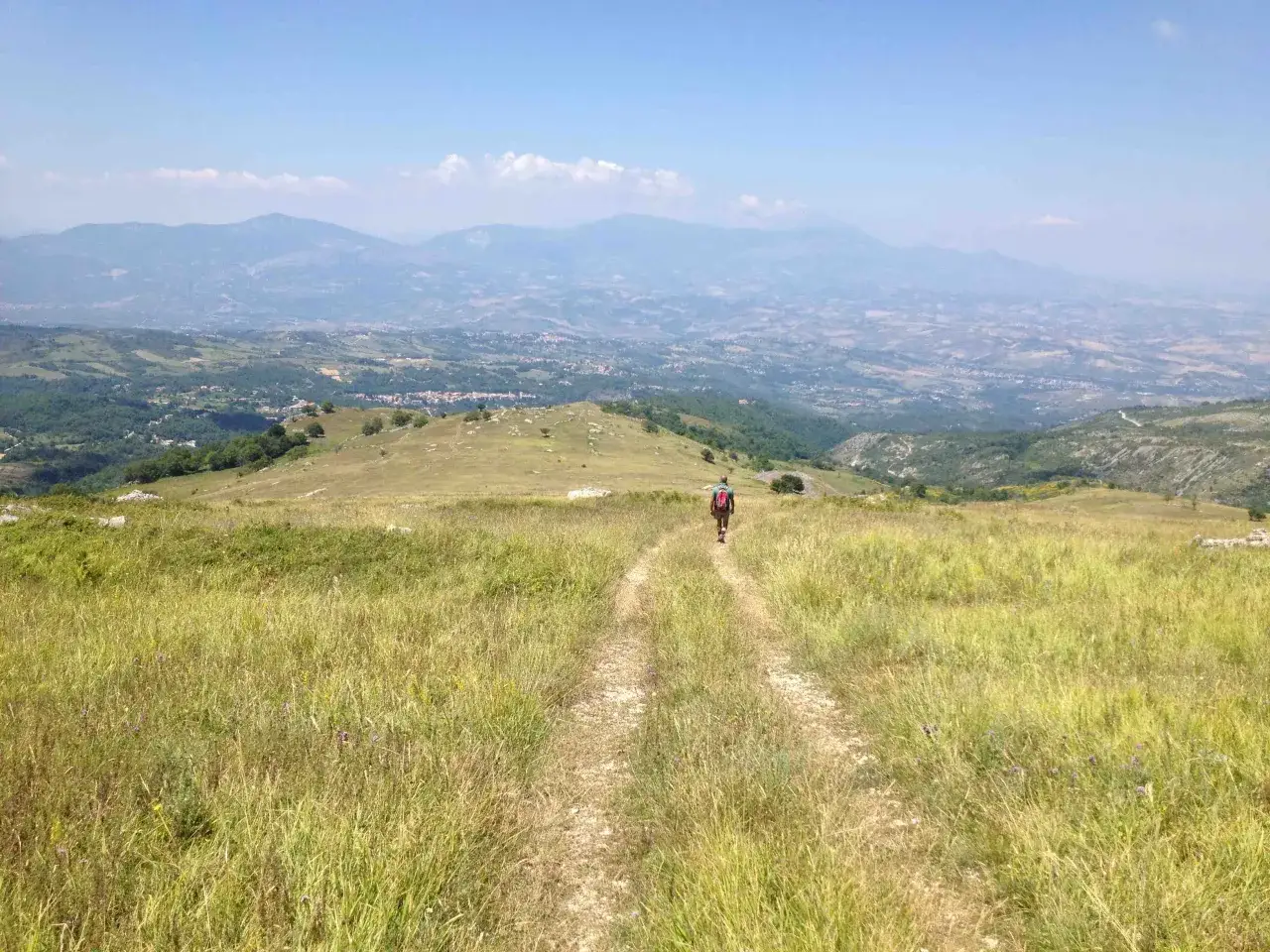 Un escursionista solitario percorre un sentiero erboso, godendosi il panorama mozzafiato di montagne e valli in una splendida giornata di **passo lanciano estate**.