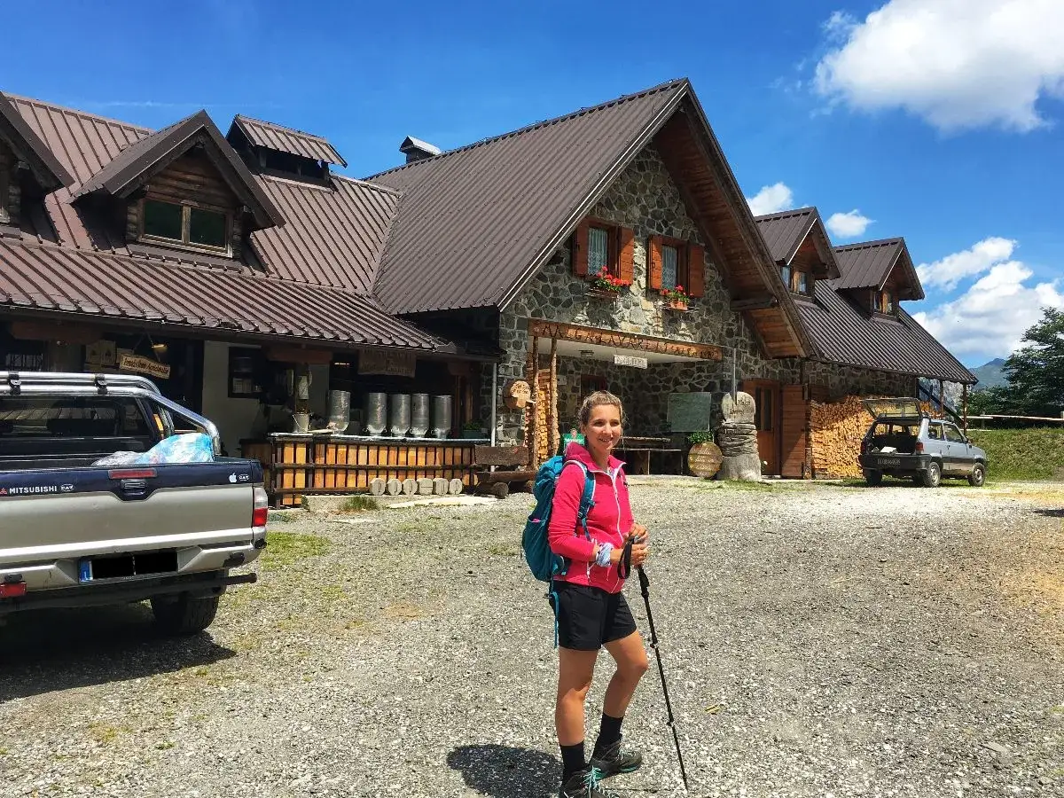 Ragazza con zaino e bastoncini da trekking davanti alla malga Lavareit, con un pick-up e un'auto parcheggiati.