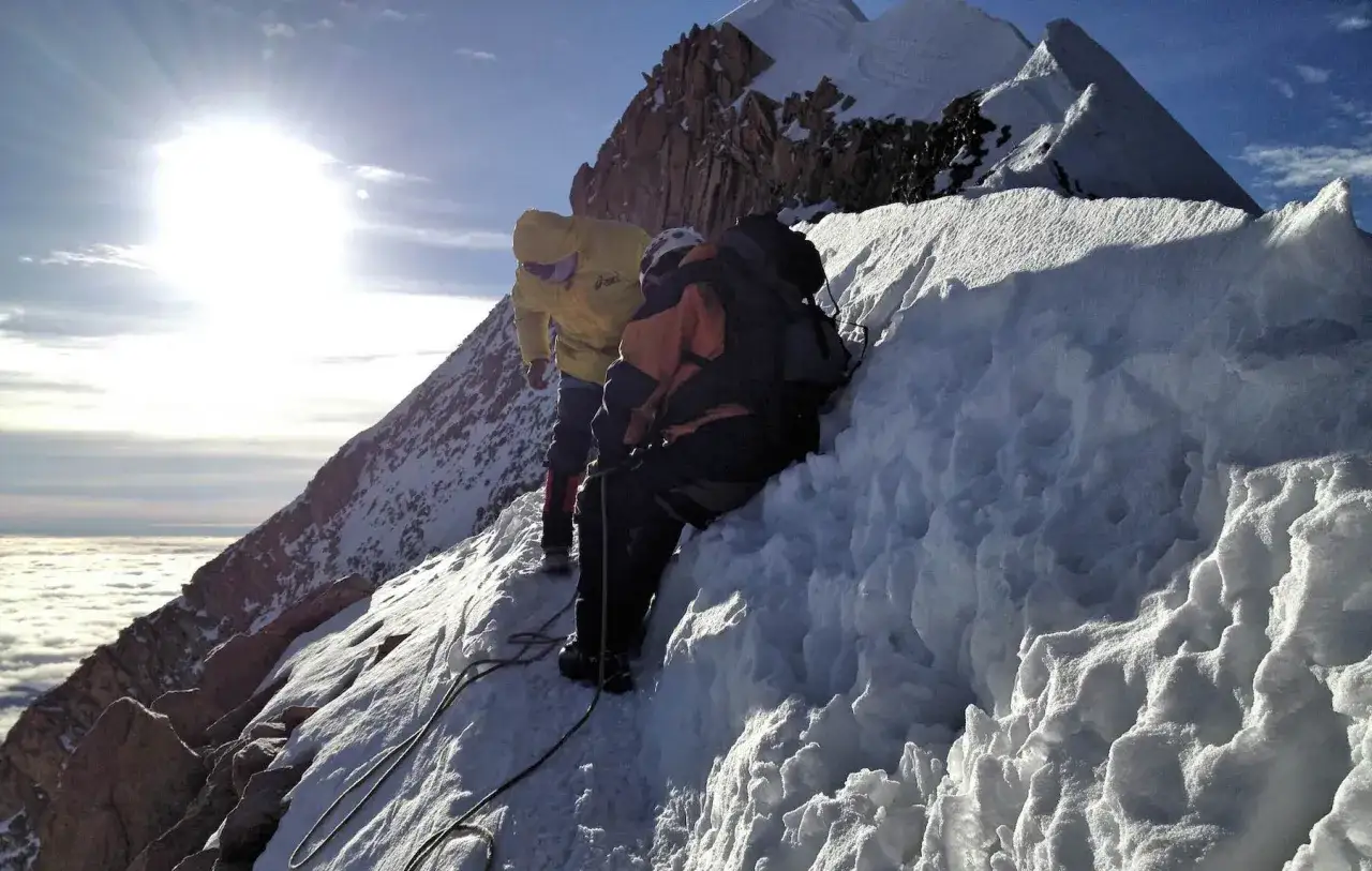 Zwei Bergsteiger auf dem Huayna Potos&iacute;, gesichert durch Seile, steigen &uuml;ber eisige H&auml;nge. &Uuml;ber ihnen strahlt die Sonne, unter ihnen eine Wolkendecke.