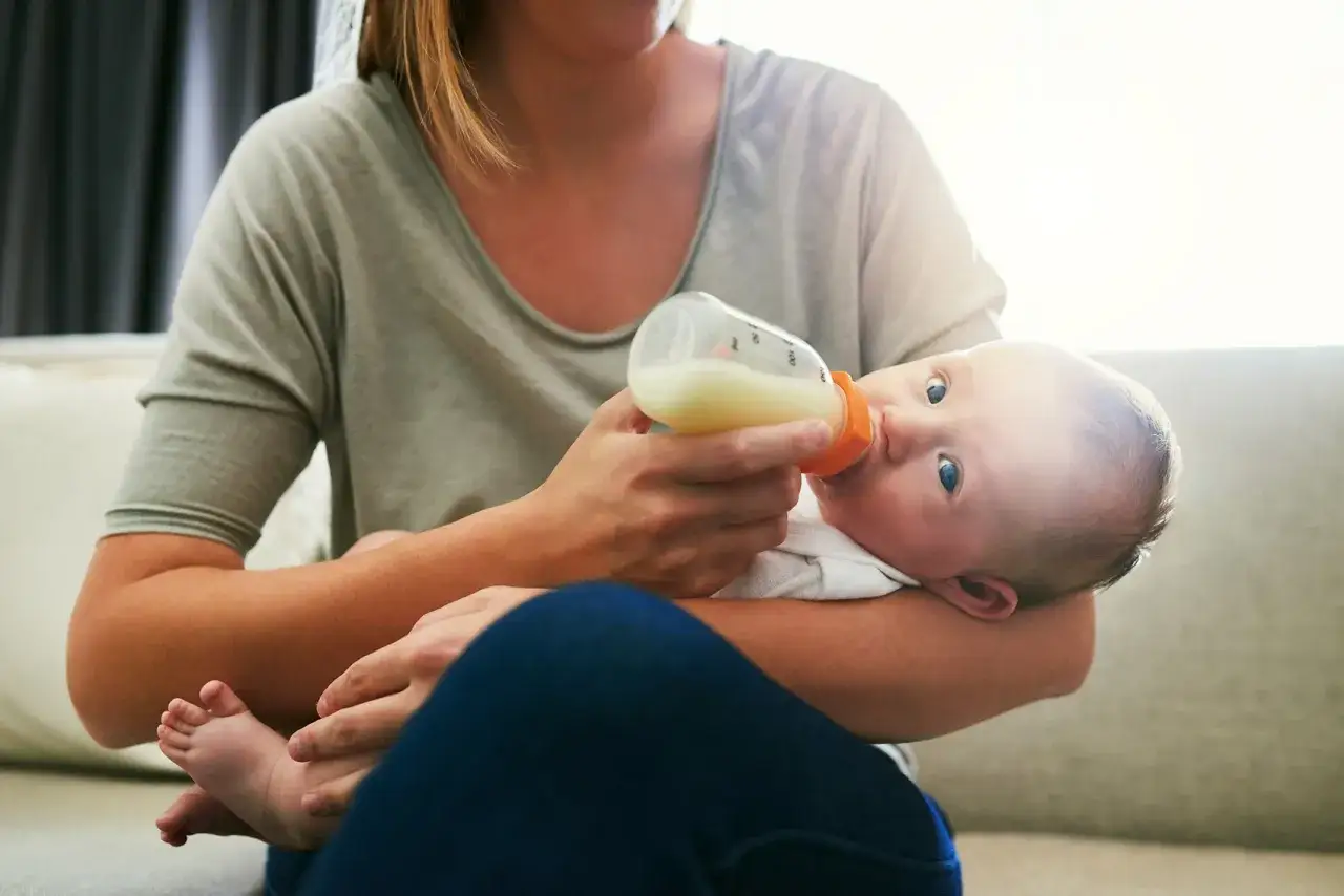 Mama karmi butelką maluszka, który uważnie patrzy. Warto wiedzieć, co ile karmić noworodka, by zapewnić mu wszystko, czego potrzebuje.