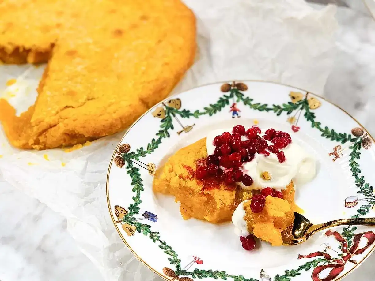En bit saffranskladdkaka utan vit choklad, toppad med vispad grädde och lingon, serveras på en julprydd tallrik.