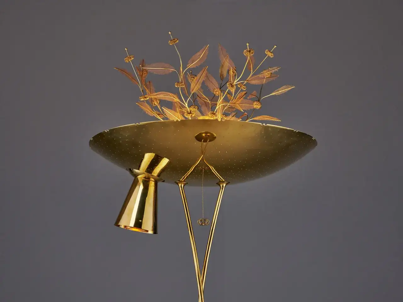 En m&auml;ssingsgolvlampa i Paavo Tynells stil, med en blomliknande dekoration av metallblad och blommor.