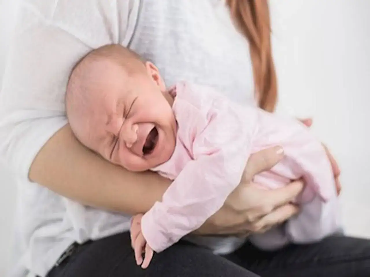 Płacz noworodka z powodu wzdętego brzucha. Mama tuli dziecko, próbując je uspokoić.