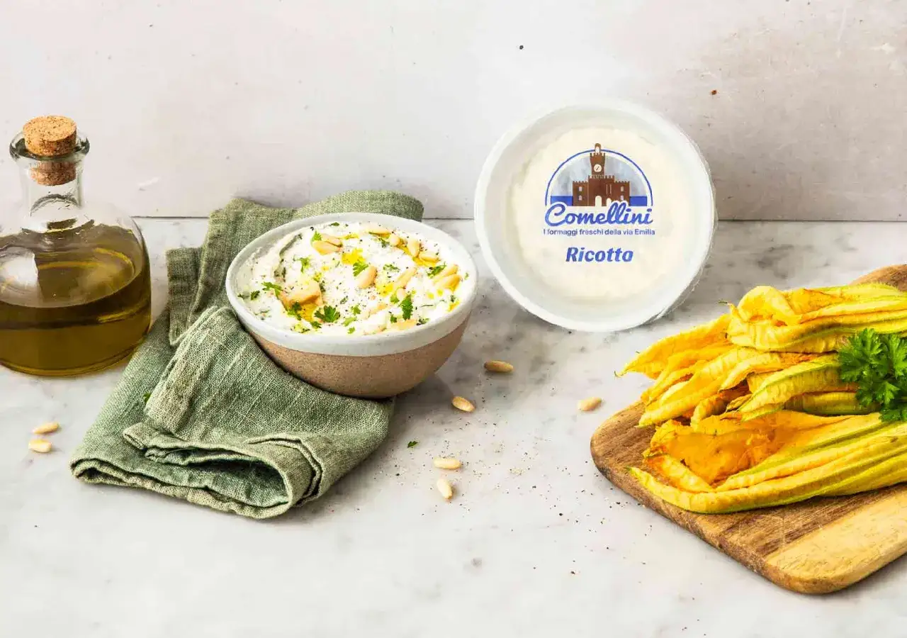 Ricotta fresca, un'ottima fonte di proteine, condita con olio, pinoli e prezzemolo, accanto a fiori di zucca.