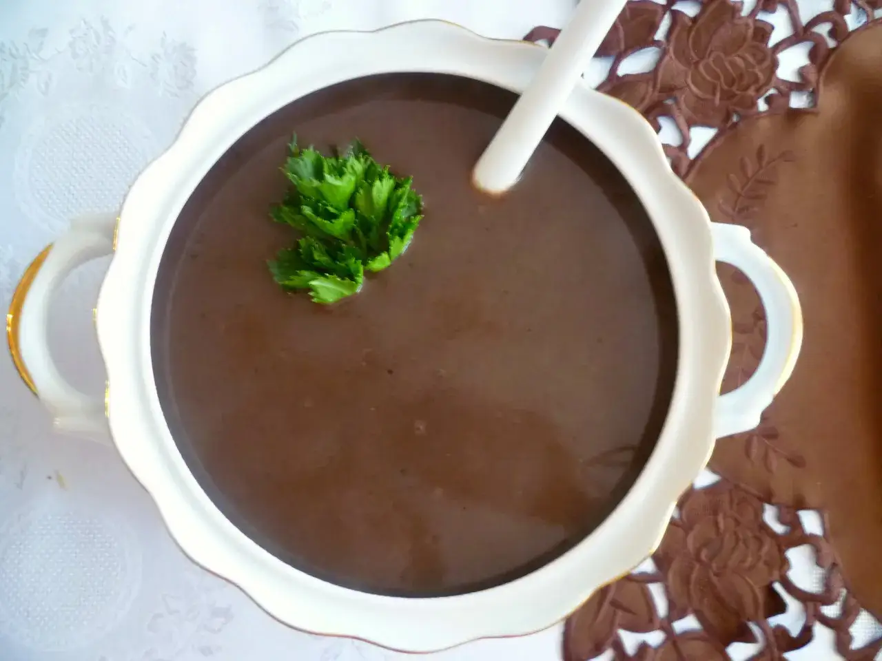 Gęsta, ciemna zupa z kaczej krwi, udekorowana natką pietruszki, podana w eleganckiej wazie.