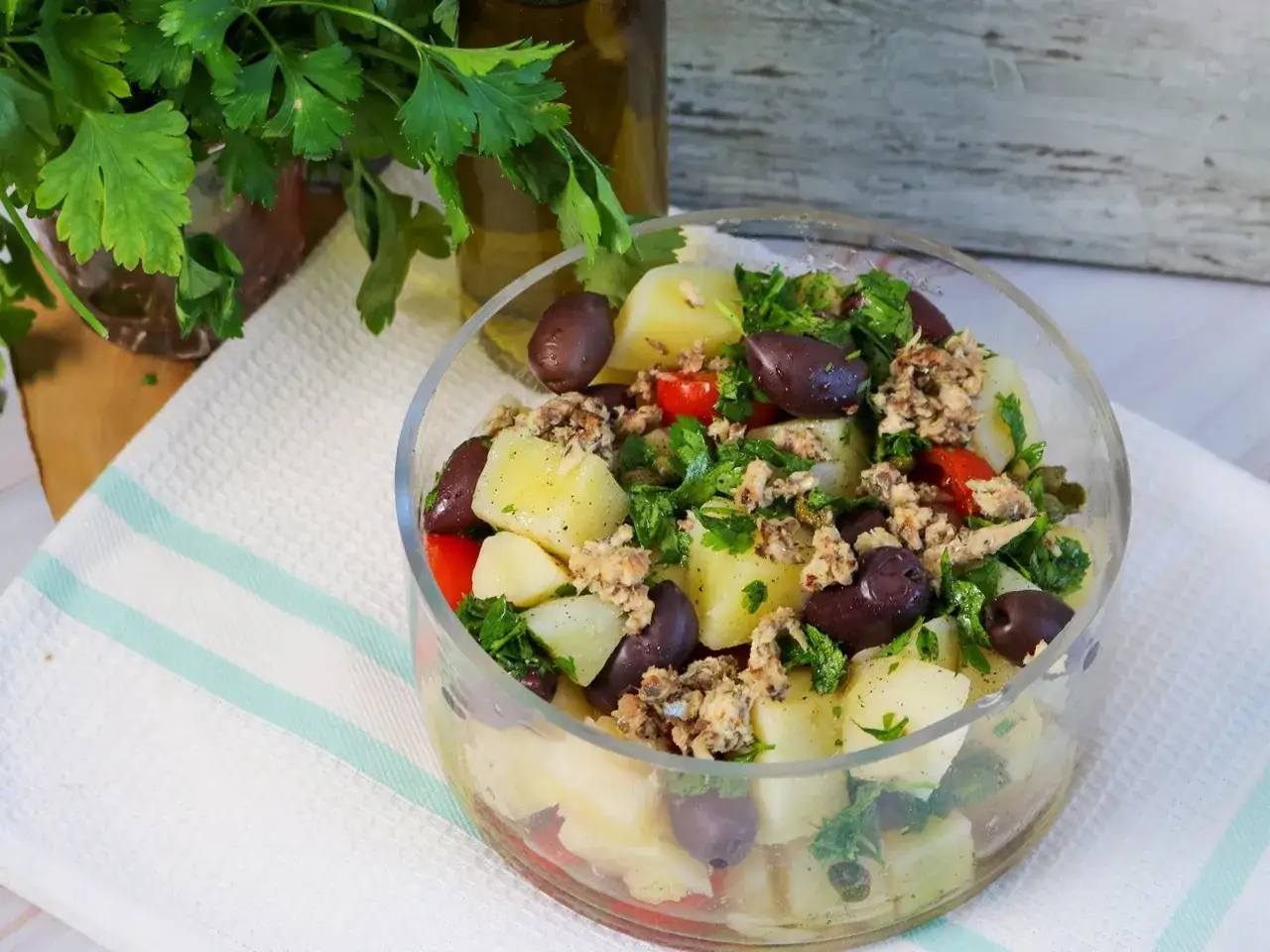 Ein k&ouml;stlicher italienischer Kartoffelsalat mit Kartoffeln, Oliven, Tomaten und frischer Petersilie, serviert in einer Glassch&uuml;ssel.