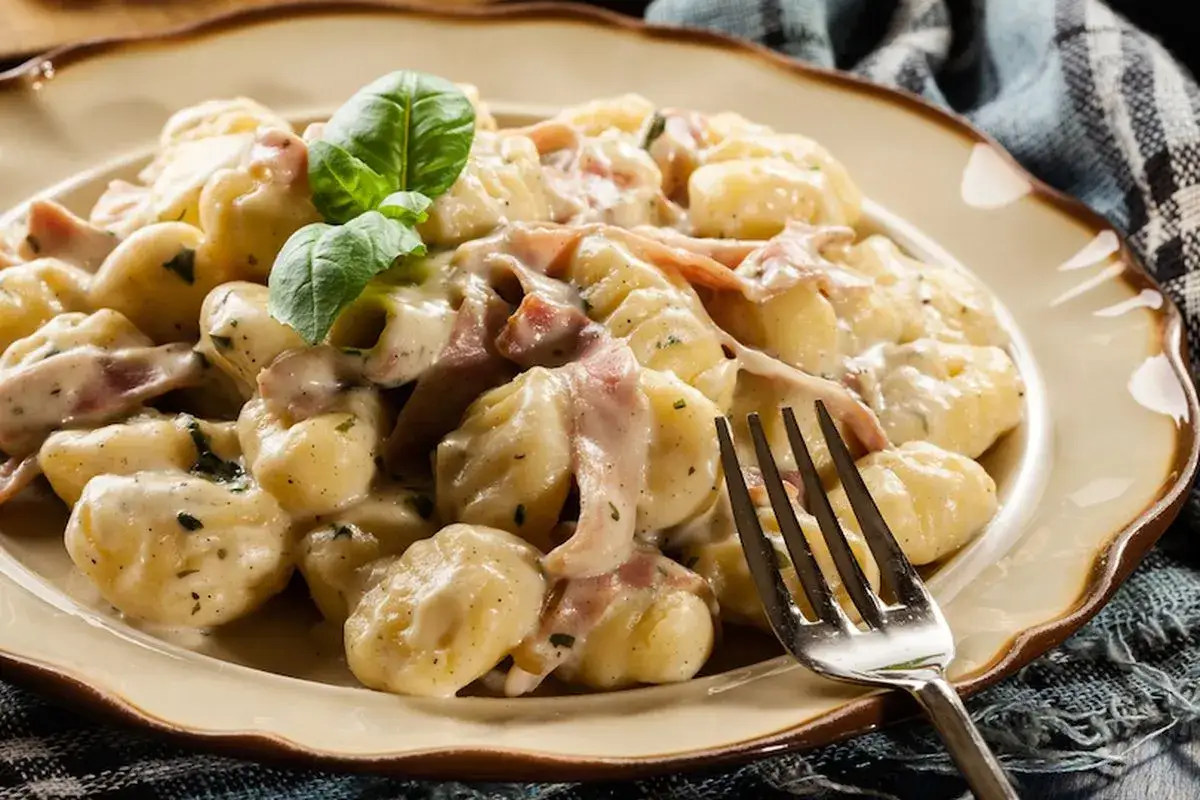 Gnocchi cremosi con prosciutto e basilico, un'idea perfetta su come condire gli gnocchi per un piatto delizioso.