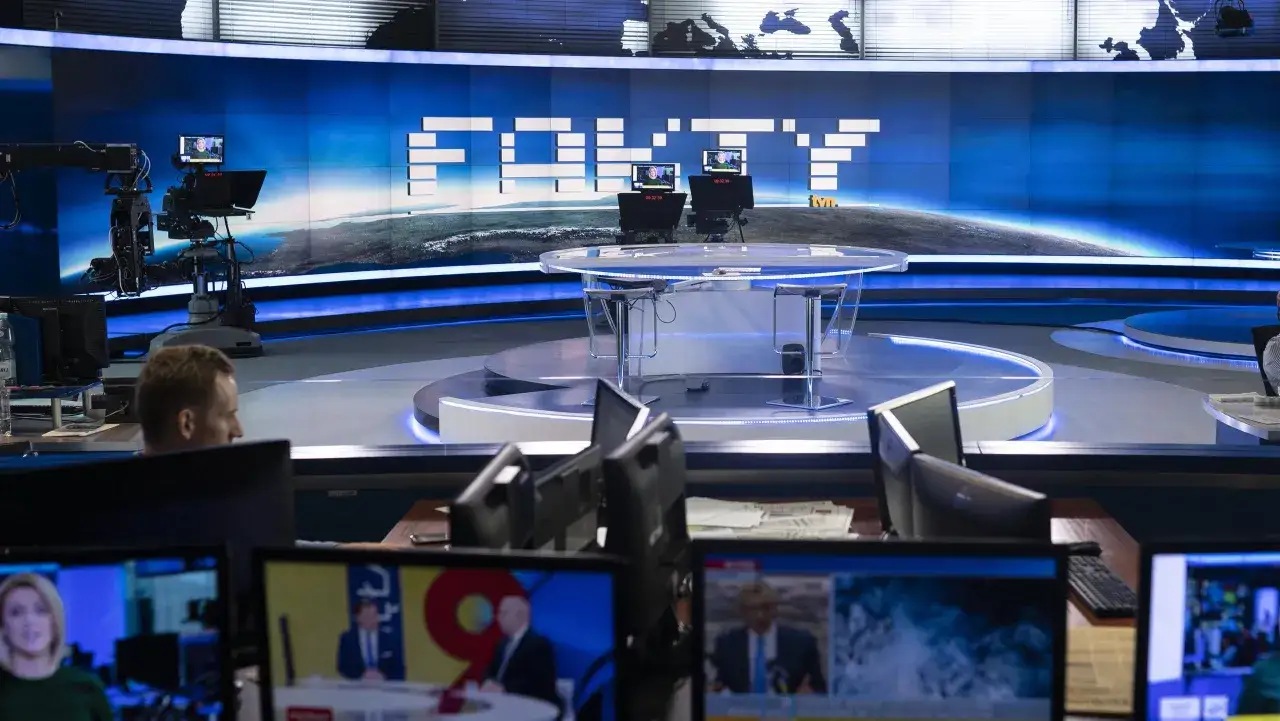 W studiu TVN Fakty ludzie przygotowują się do wydania wiadomości. W tle widać wielki ekran z logo i globusem.