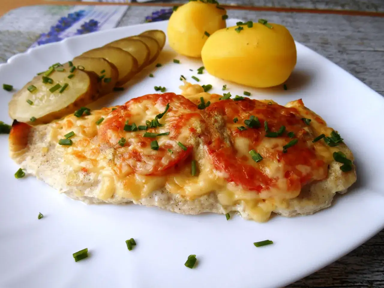 Pyszna pierś z kurczaka z serem i pomidorami, podana z ziemniakami i szczypiorkiem.