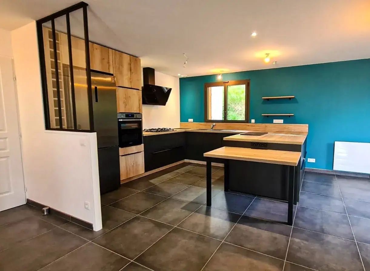 Cuisine moderne en 2 parties, avec îlot central en bois et noir, murs bleu canard et éléments en bois clair.