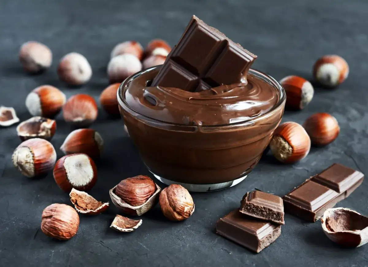 Aksamitny krem gianduja w miseczce, otoczony orzechami laskowymi i kawałkami czekolady.