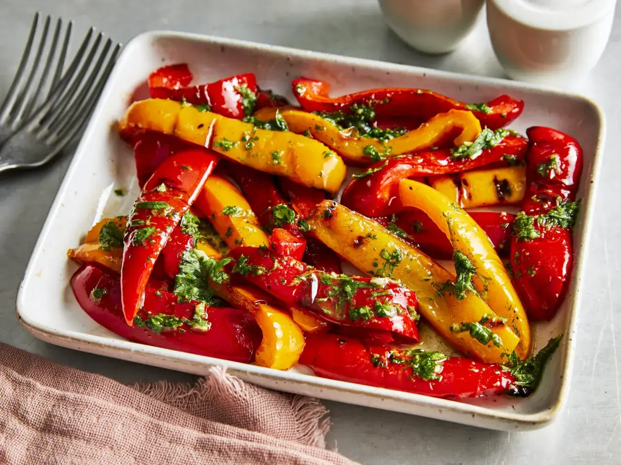 Saftige, gegrillte Paprika in Rot und Gelb, mariniert mit Kräutern, serviert in einer weißen Schale.