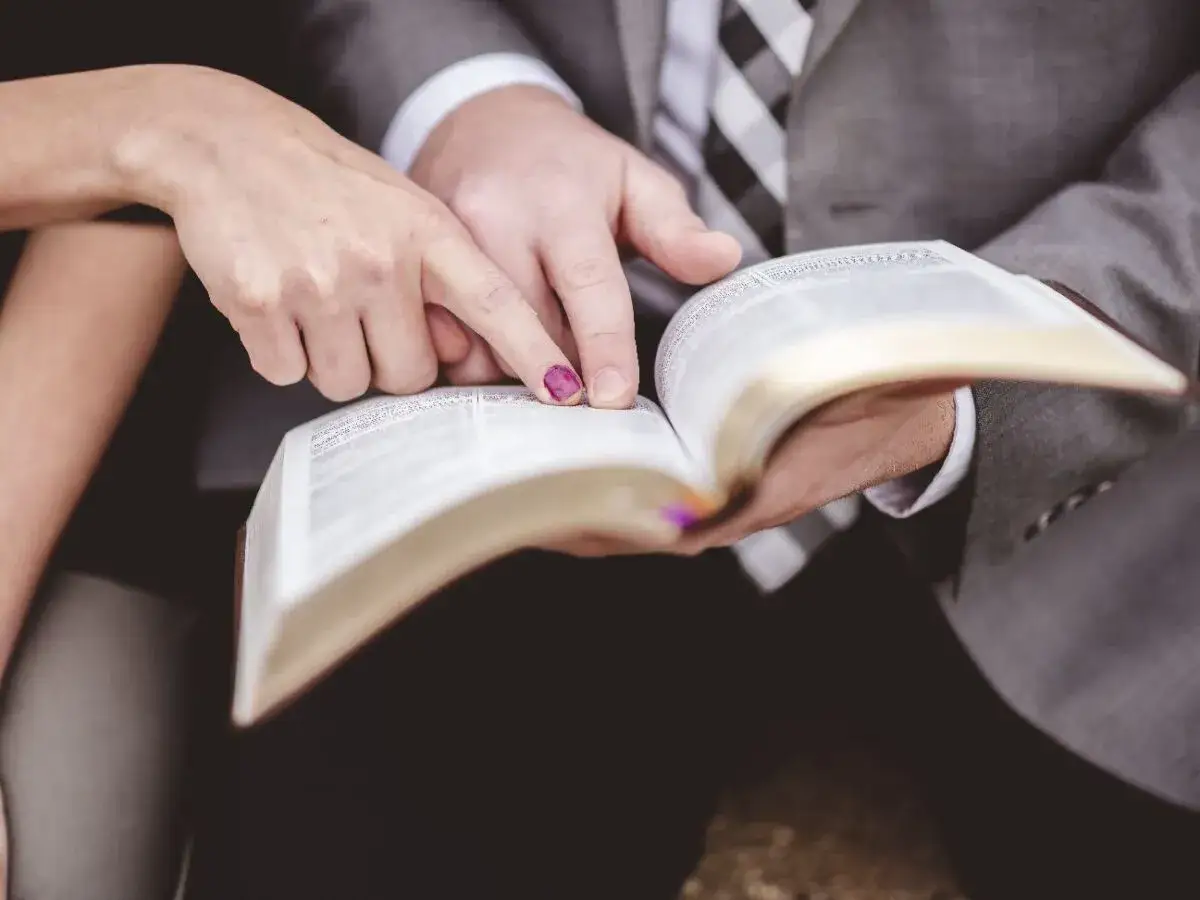 Dłoń kobiety i mężczyzny wskazują na tekst w Biblii, przygotowując się do ślubnych czytań.
