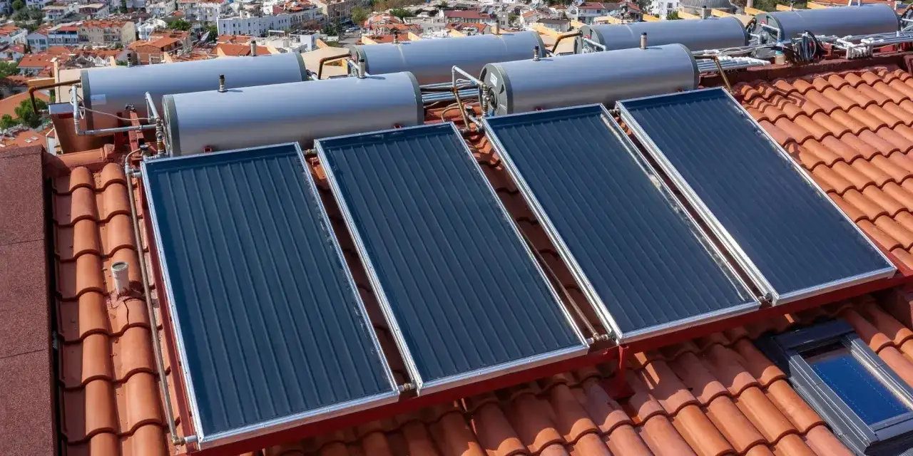 Sur un toit de tuiles, plusieurs panneaux solaires thermiques sont install&eacute;s, connect&eacute;s &agrave; des chauffe-eau.