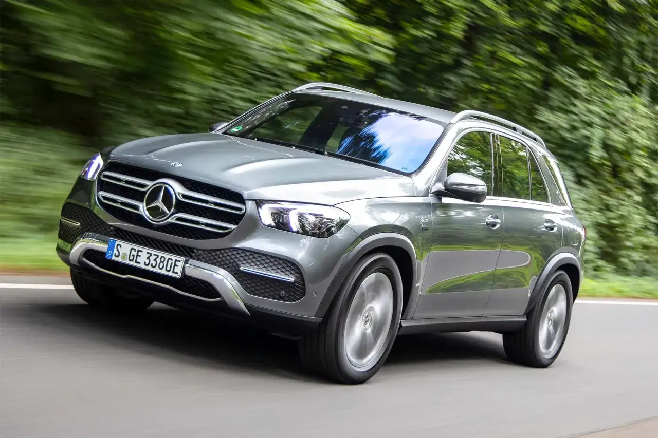 Silberner Mercedes-Benz GLE 350de f&auml;hrt auf einer Stra&szlig;e durch gr&uuml;nen Wald.