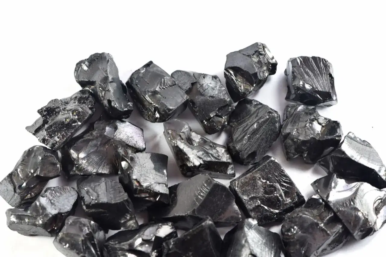 Mont&oacute;n de piedras negras brillantes, con reflejos met&aacute;licos, que muestran las **shungita propiedades** de este mineral &uacute;nico.
