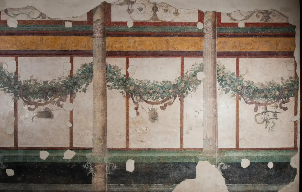 Affresco nella casa di Livia: ghirlande di frutta e fiori adornano le pareti, con colonne dipinte che creano un senso di profondità.