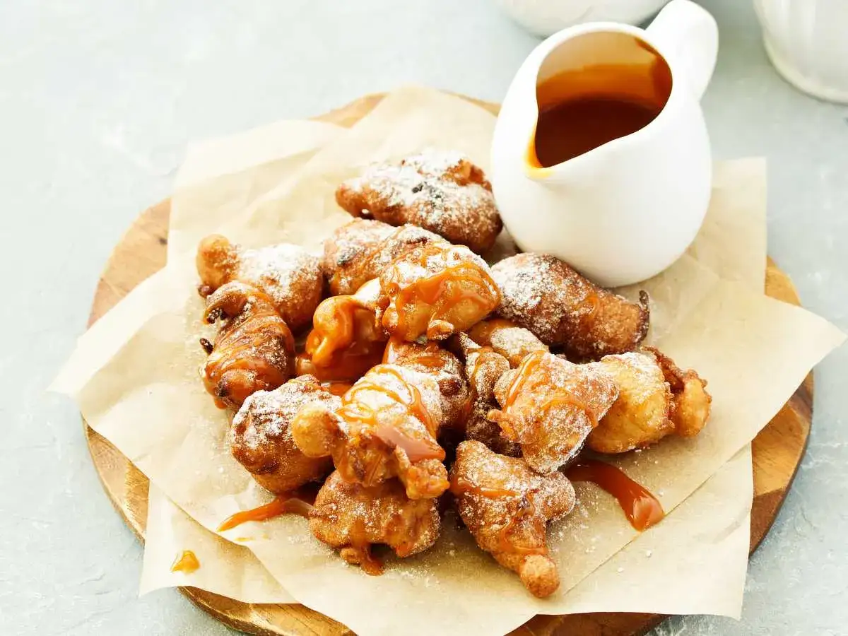 Deliciosos buñuelos de manzana cubiertos con azúcar glas y un chorrito de salsa de caramelo.