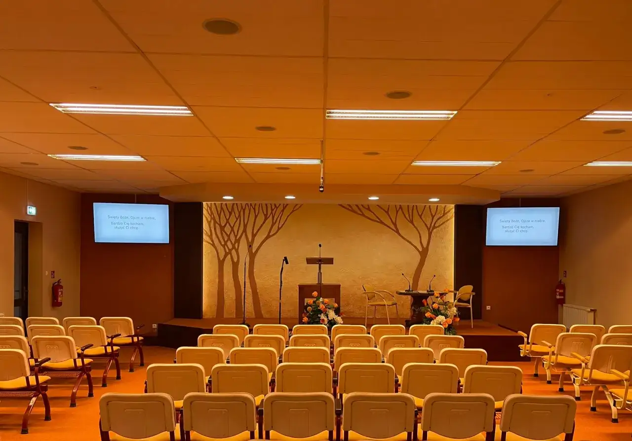 An empty Kingdom Hall, a place of worship for Jehovah's Witnesses, with rows of chairs facing a stage.