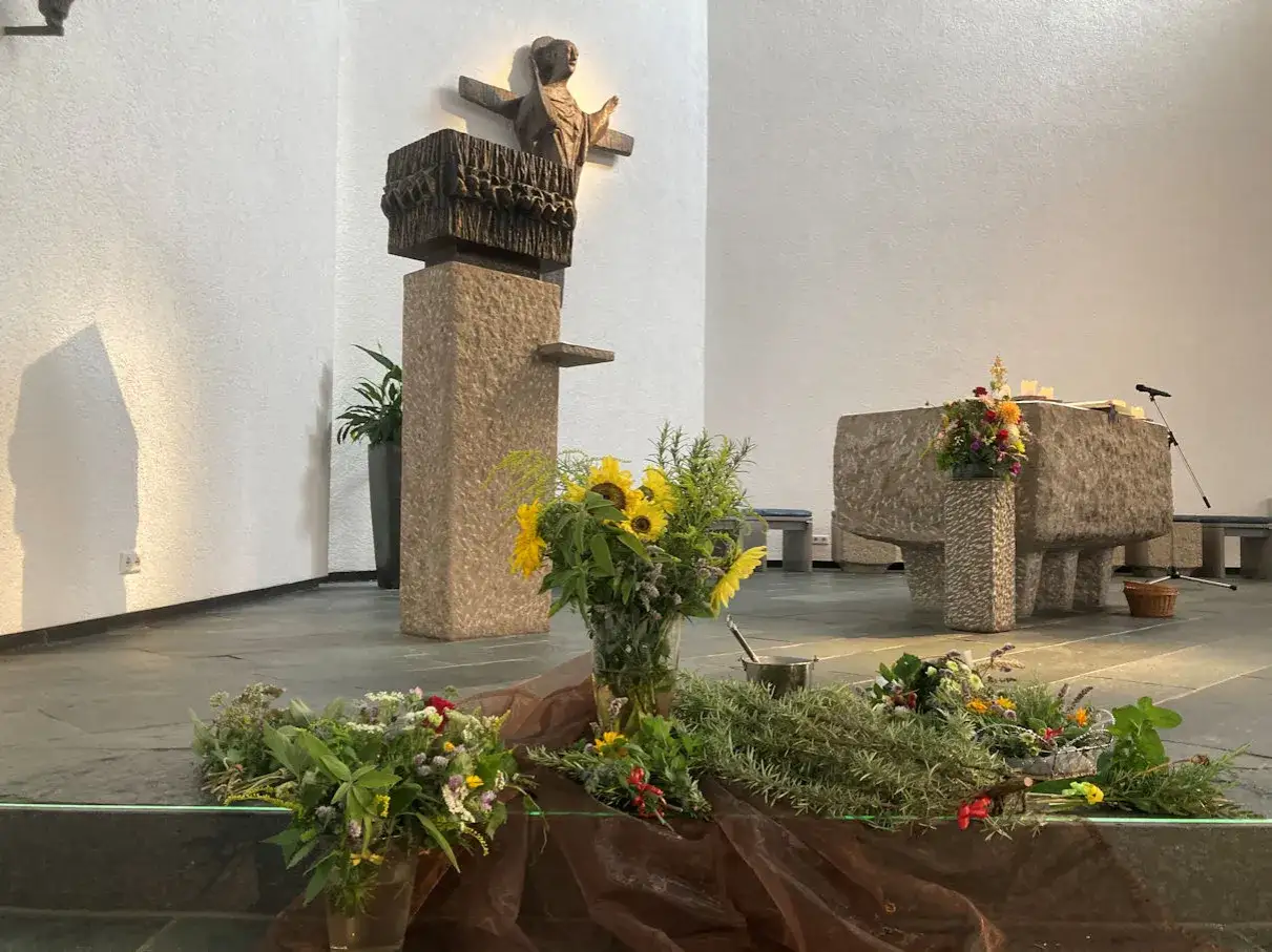 Blumen geschmücken den Altar in der Kirche. Ein Kreuz mit einer Figur erinnert an Maria Himmelfahrt.