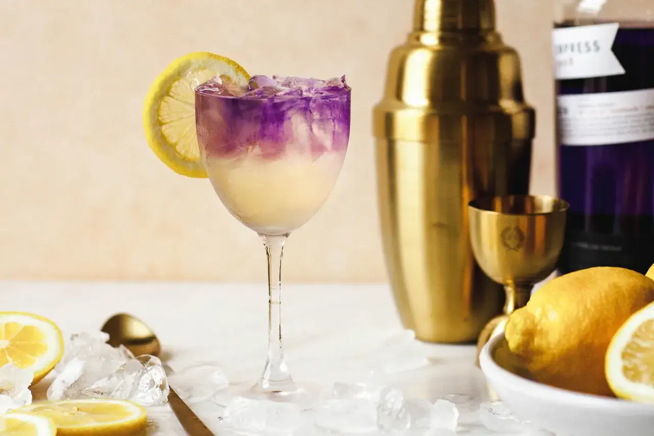 En vacker lila och gul drink med is och citronskiva, redo att avnjutas som en elderflower sour.