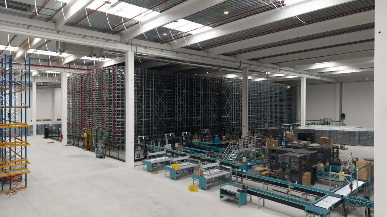 Magazzino automatizzato con scaffalature alte, nastri trasportatori e macchinari per la logistica, esempio di **economia di scala**.