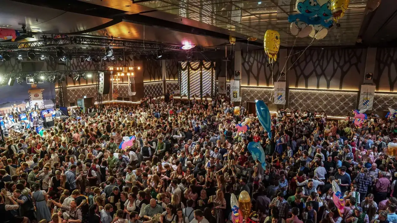 Volles Festzelt beim Starkbierfest Nockherberg. Menschen in Tracht feiern ausgelassen, mit Bierkr&uuml;gen in den H&auml;nden und bunten Ballons &uuml;ber ihnen.