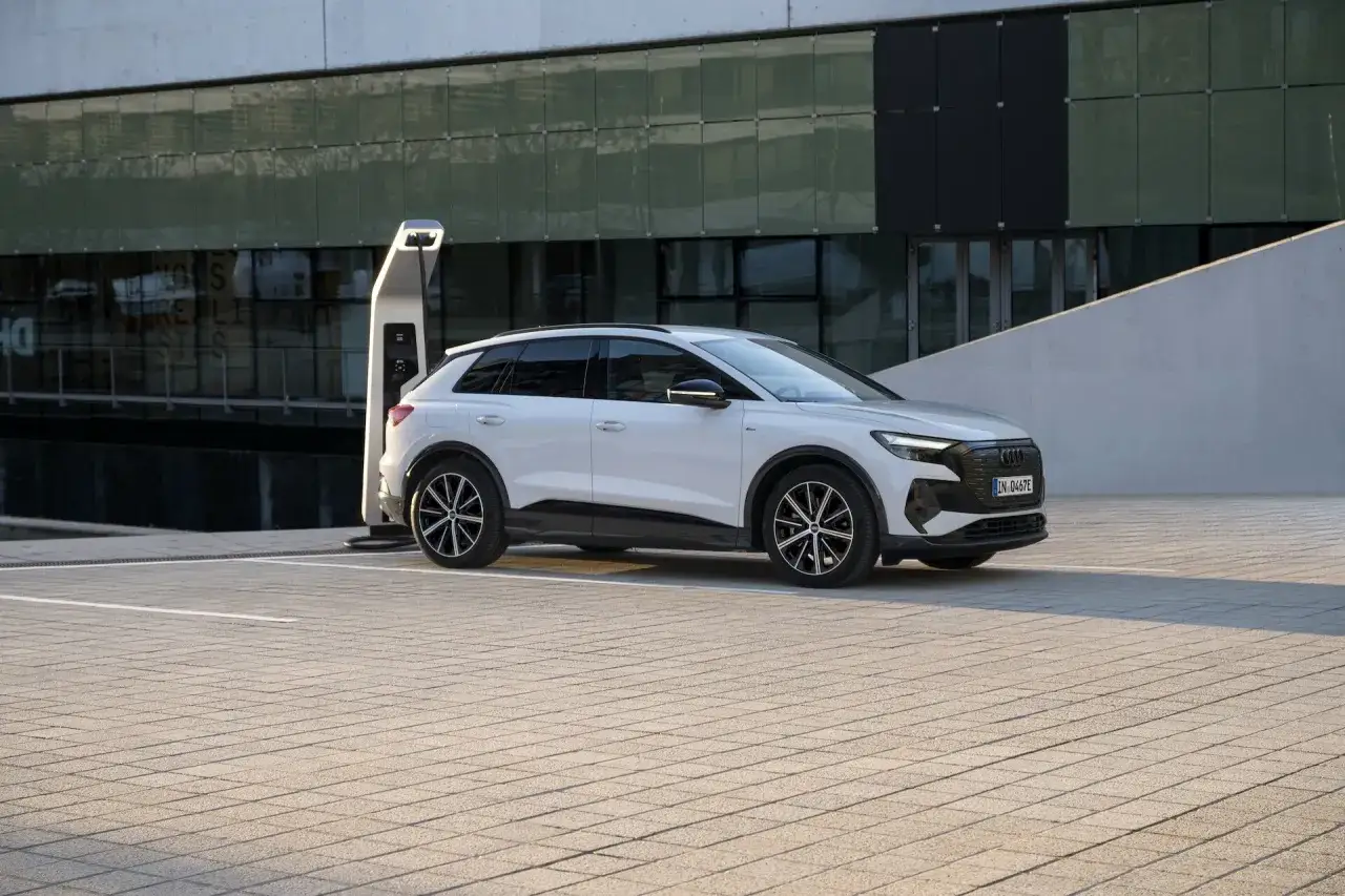 Biały Audi Q4 elektryk zaparkowany przy ładowarce na tle nowoczesnego budynku.
