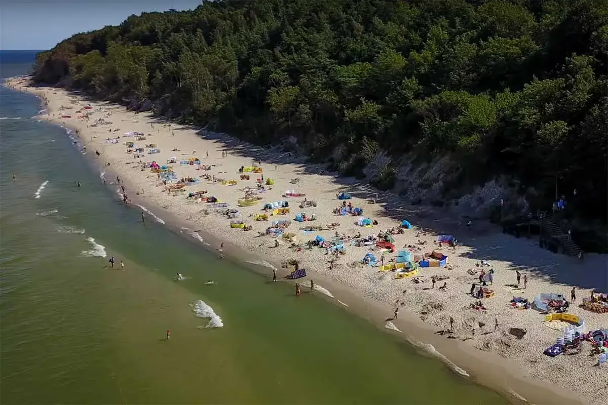 Plaża w Jastrzębiej Górze, najbardziej wysuniętym mieście na północ Polski. Tłumy plażowiczów, kolorowe parawany i zielony las na klifie.