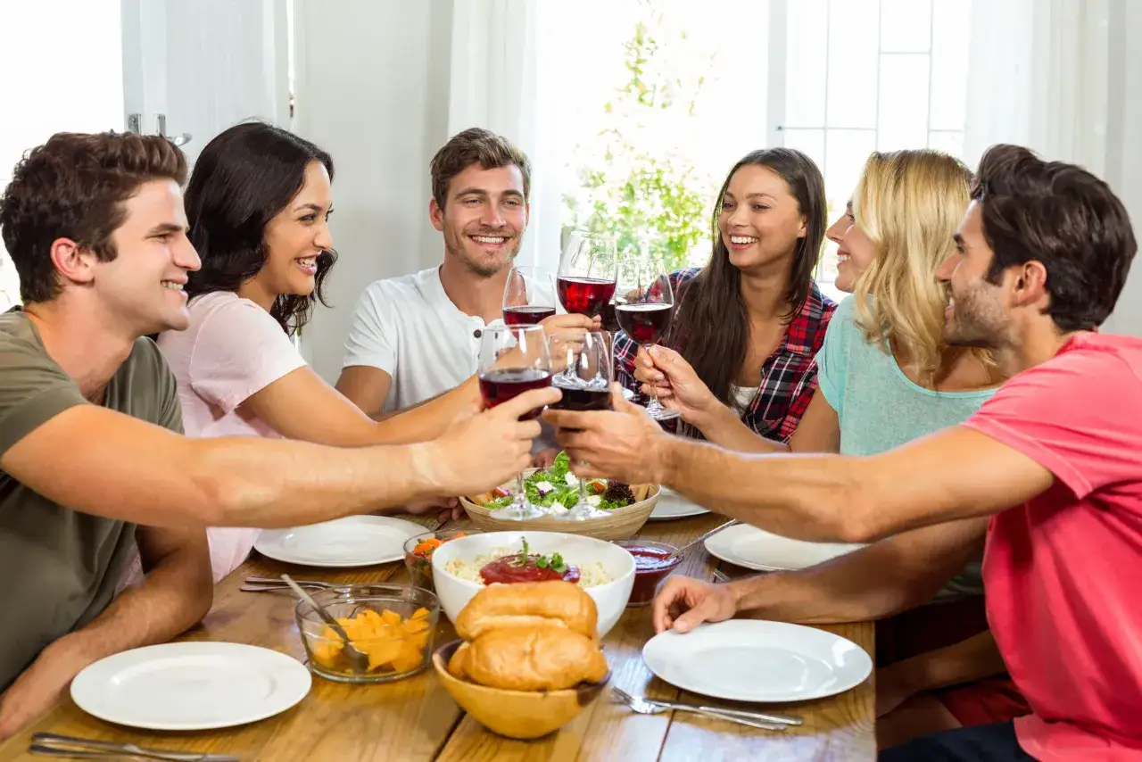Amigos brindan con vino tinto, disfrutando de una comida que evoca 10 tradiciones francesas: la buena compañía, la gastronomía y la celebración.