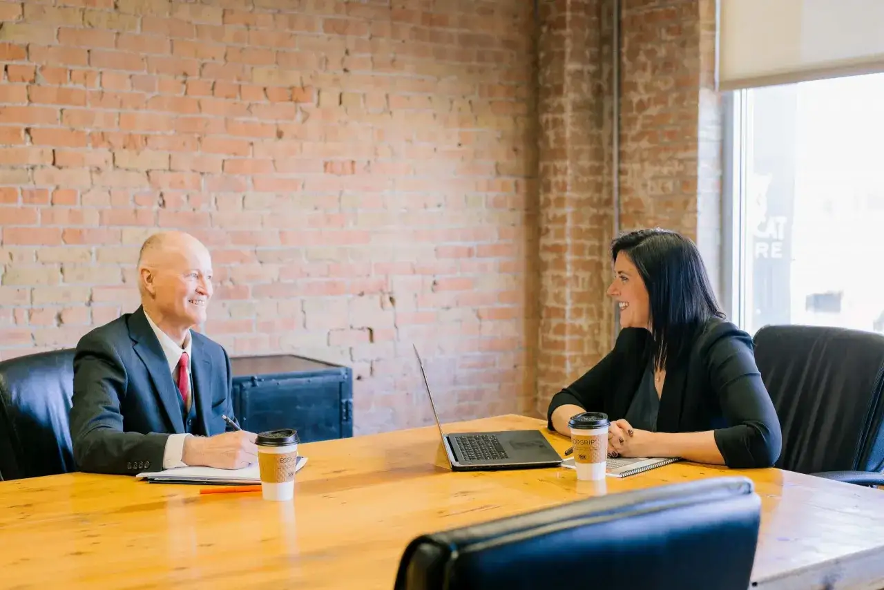 A man and woman smile at each other across a table, discussing performance review examples.