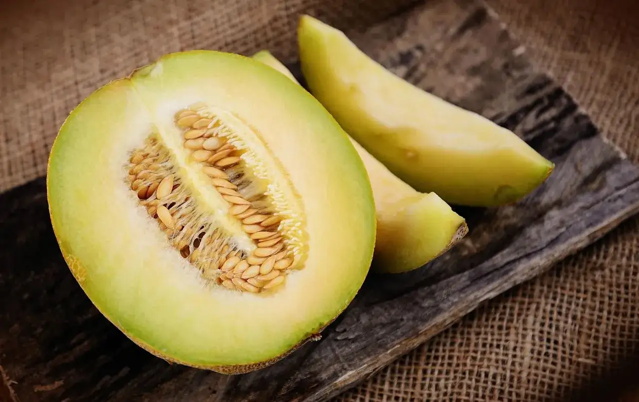 Poł&oacute;wka i kawałki melona na drewnianej desce. Nasiona widoczne w środku. Melon ma niski indeks glikemiczny.