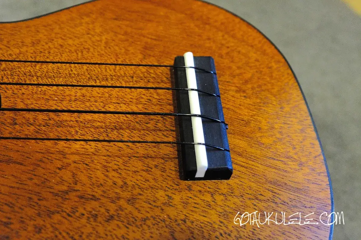 Nahaufnahme des Stegs einer Ukulele mit vier schwarzen Saiten. Die ukulele saiten dicke variiert leicht, was f&uuml;r den Klang wichtig ist.
