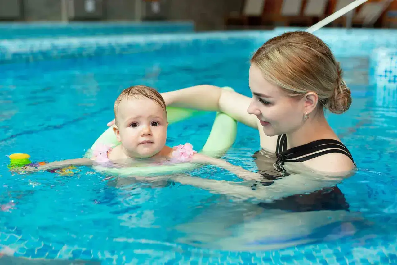 Mama uczy dziecko pływać w basenie. Niemowlę w kółku pływackim, mama z uśmiechem wspiera je w wodzie.