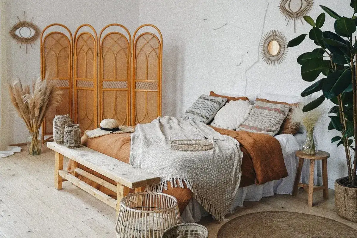 Przytulna sypialnia w stylu boho z plecionym parawanem, łóżkiem w kolorze cegły i mnóstwem naturalnych tekstur.