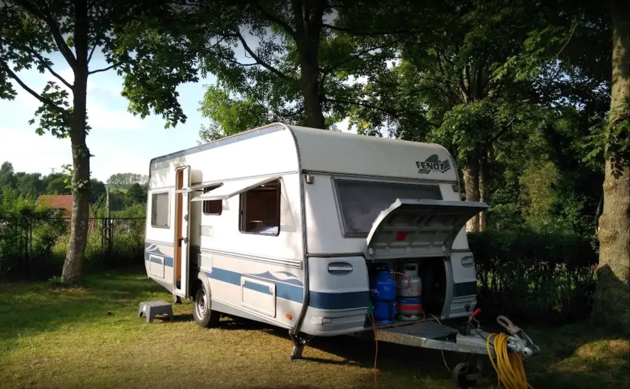 Przygotowania do wypoczynku na **camping Duszniki Zdrój**. Przyczepa kempingowa z otwartym tyłem, widoczne butle gazowe.