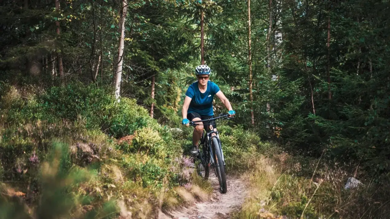 Kvinna cyklar p&aring; en stig i skogen, njuter av mtb i Falun.