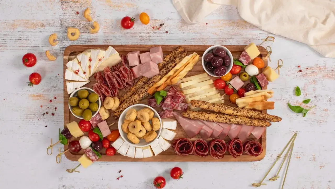 Un invitante tagliere salumi e formaggi con olive, pomodorini, taralli e grissini, perfetto per un aperitivo.