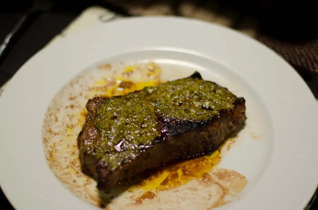 En saftig biff med gr&ouml;n topping, serverad p&aring; en vit tallrik. En klassisk r&auml;tt som p&aring;minner om en m&aring;ltid p&aring; cafe de Paris.