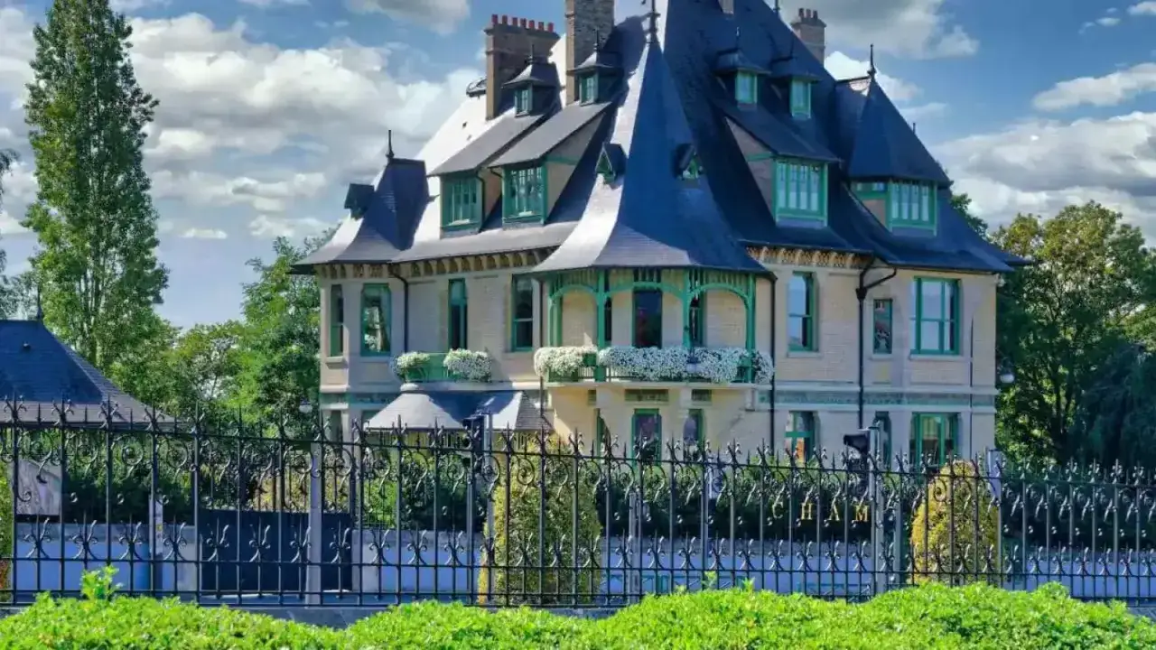 La villa Demoiselle à Reims, une demeure de caractère avec ses toits pointus et ses balcons fleuris, se dresse fièrement derrière une grille ouvragée.