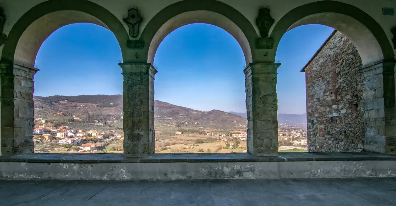 Archi in pietra incorniciano un panorama collinare con borghi e uliveti, un invito a scoprire cosa vedere a Castiglion Fiorentino.