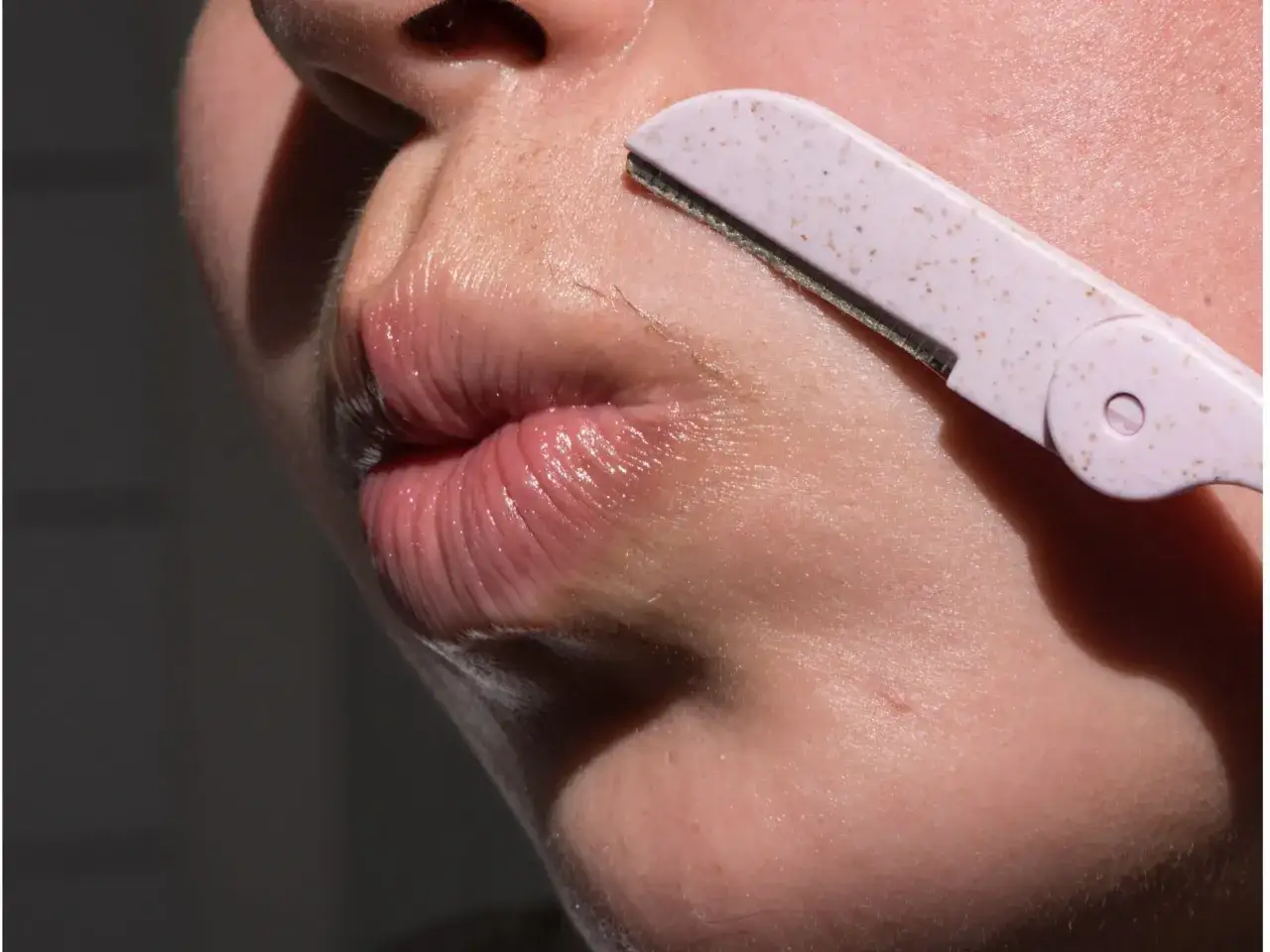 N&auml;rbild p&aring; en person som rakar sin raka mustasch med en liten rosa rakhyvel.