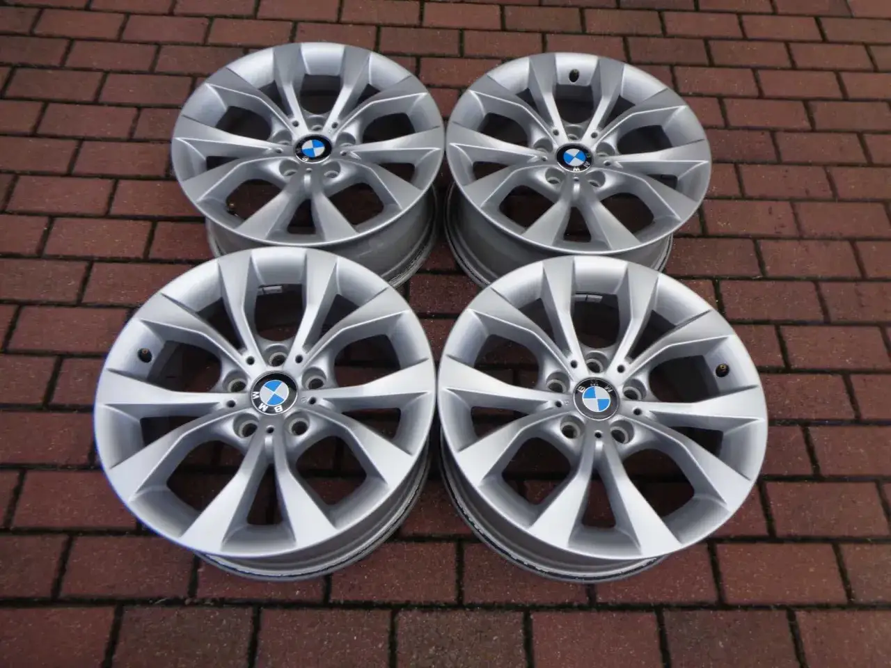 Cztery felgi aluminiowe do BMW 520d xDrive, z logo BMW, leżą na ceglanej nawierzchni.
